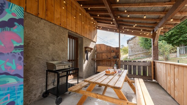Un'area esterna coperta con tavolo e panche in legno, un barbecue e un muro decorato con graffiti.