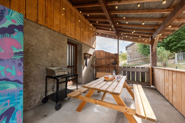 A covered outdoor area with a wooden table and benches, a grill, and a wall with a graffiti design.
