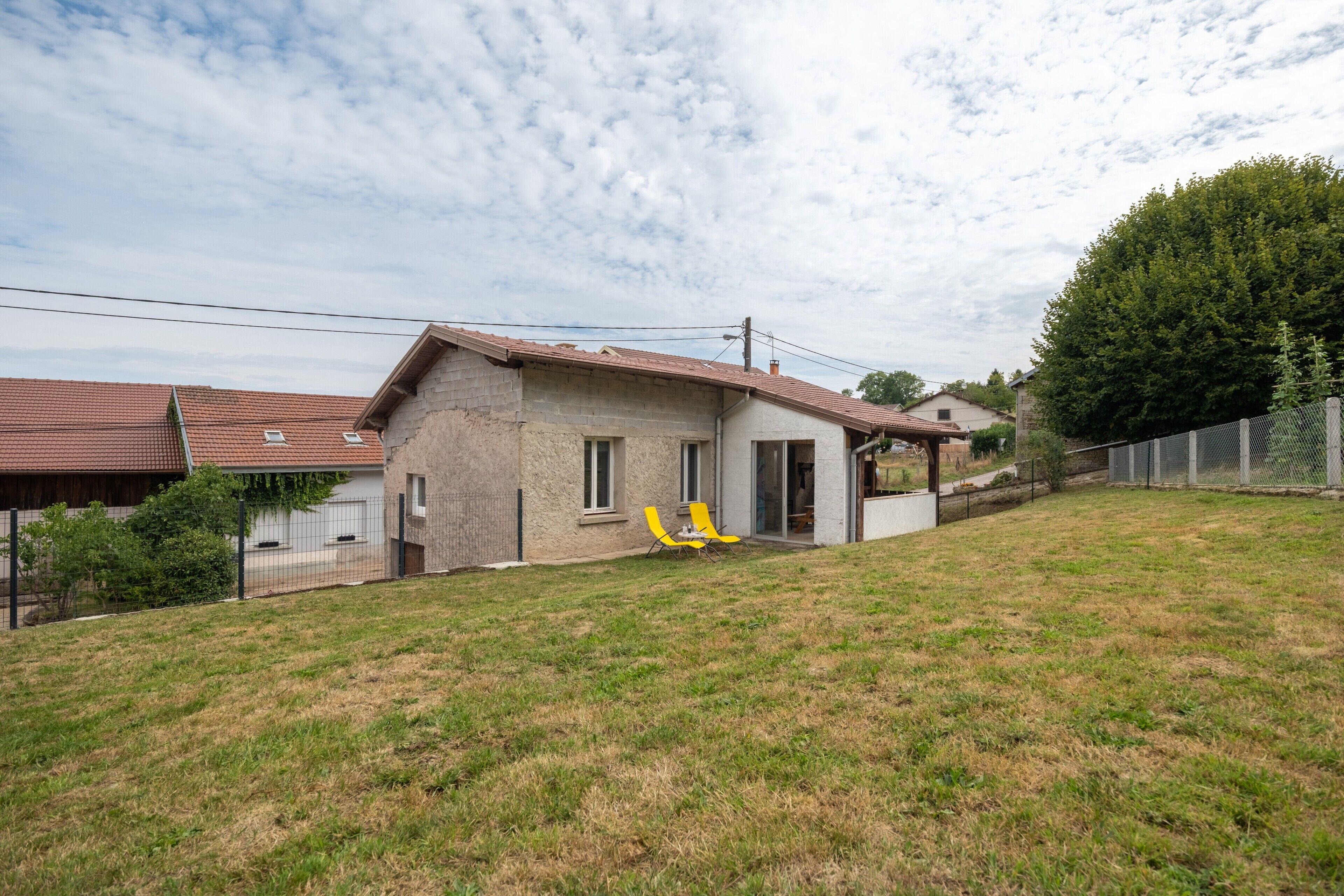Une maison de plain-pied avec un toit en pente, un petit porche et une cour gazonnée.