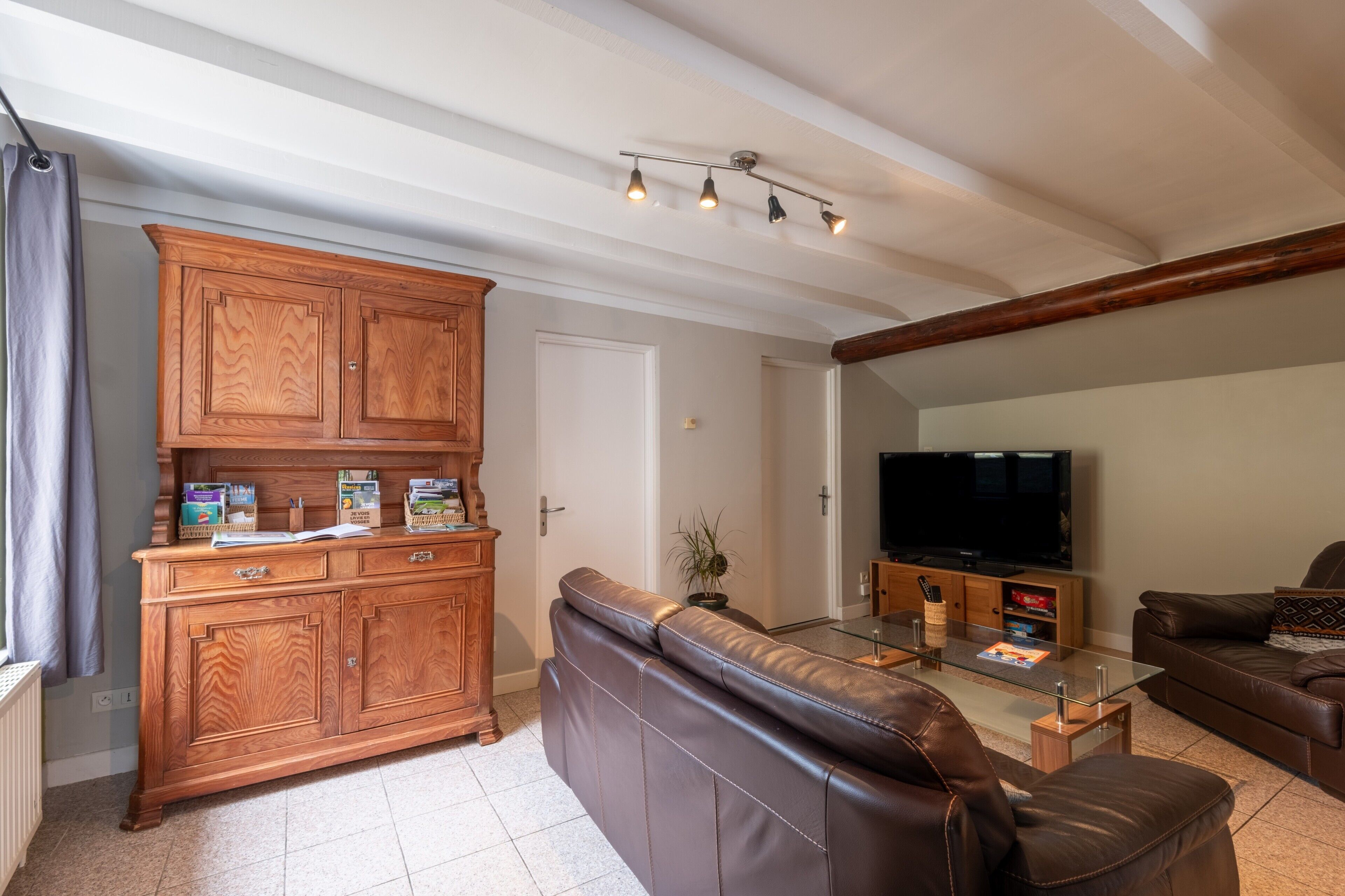 A living room with a wooden cabinet, leather sofa, glass coffee table, and a flat-screen TV.