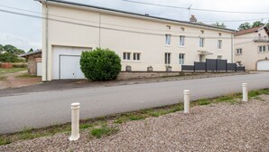 A two-story building with a garage, a small garden, and a paved driveway. - La Grande Escapade Holiday Home – 6 Guests (Up to 10 on Request), Countryside View, Terrace, Wi-Fi (Xertigny)