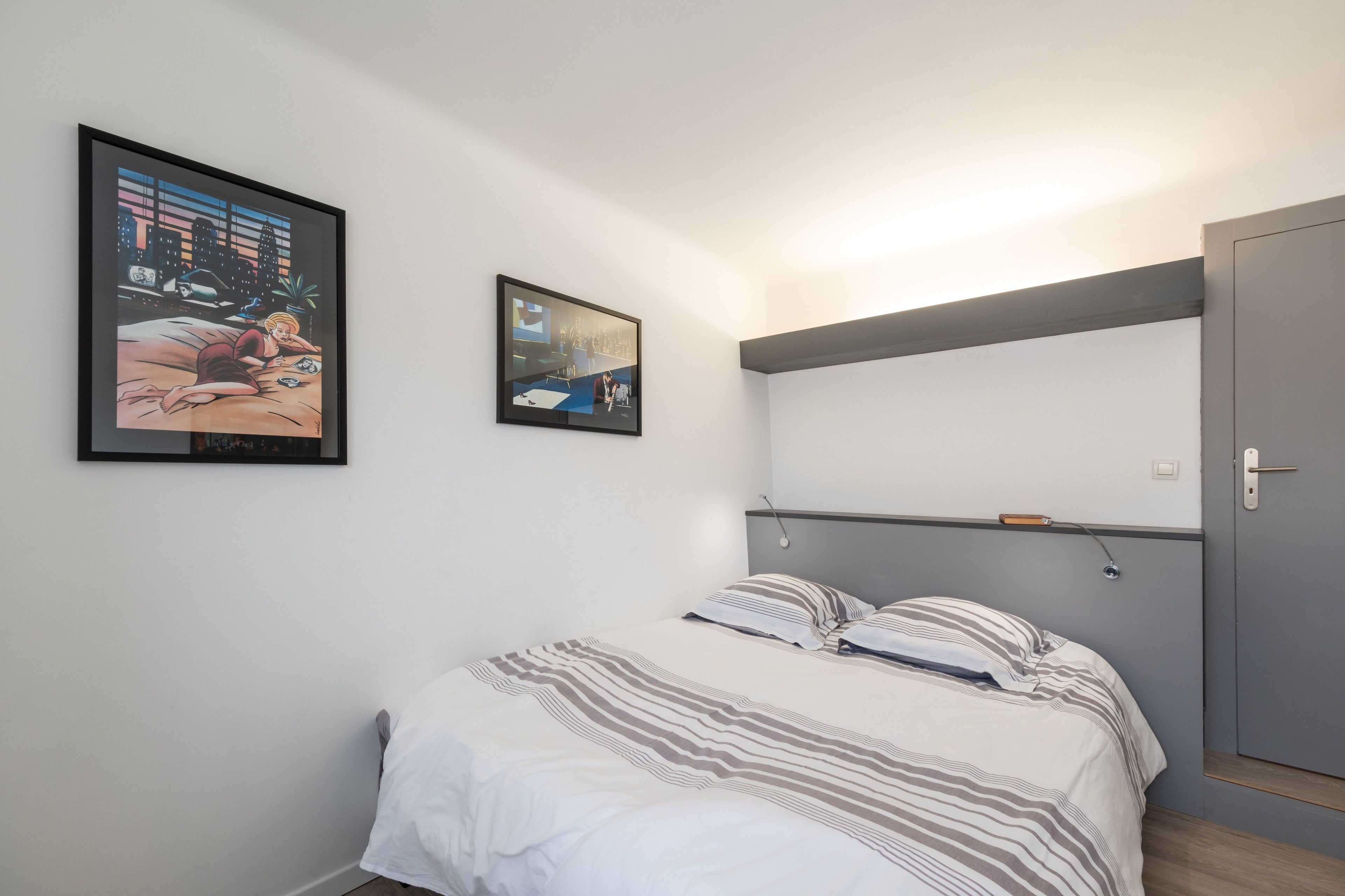 Quarto com cama, duas obras de arte emolduradas, mesa de cabeceira e guarda-roupa.