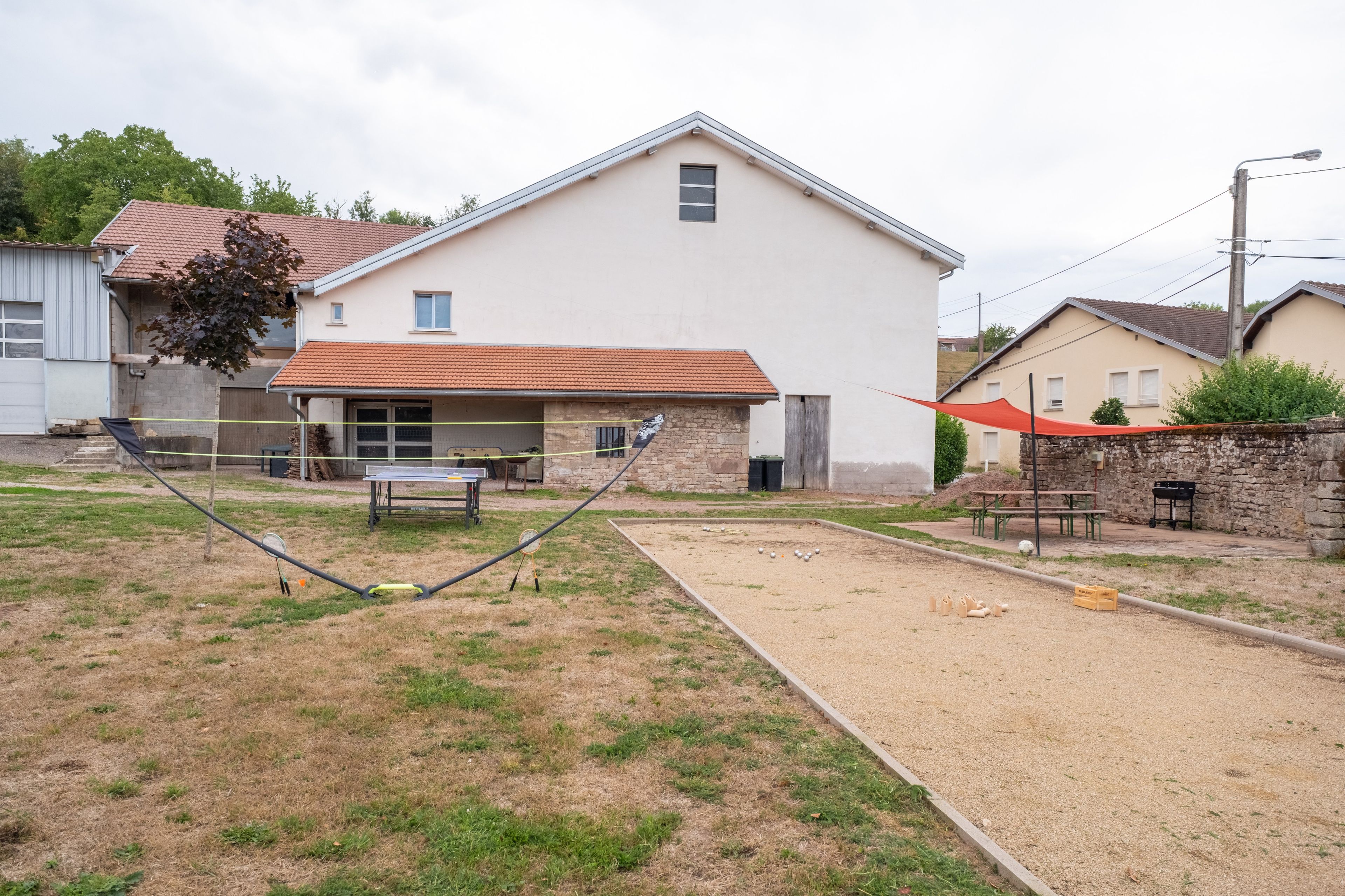 A residential area with a house, a tennis court, and a barbecue setup.
