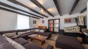 Un salon moderne avec un canapé d’angle, une table basse et une cheminée. Des tableaux encadrés ornent le mur, et une porte à panneaux de verre est également présente.
