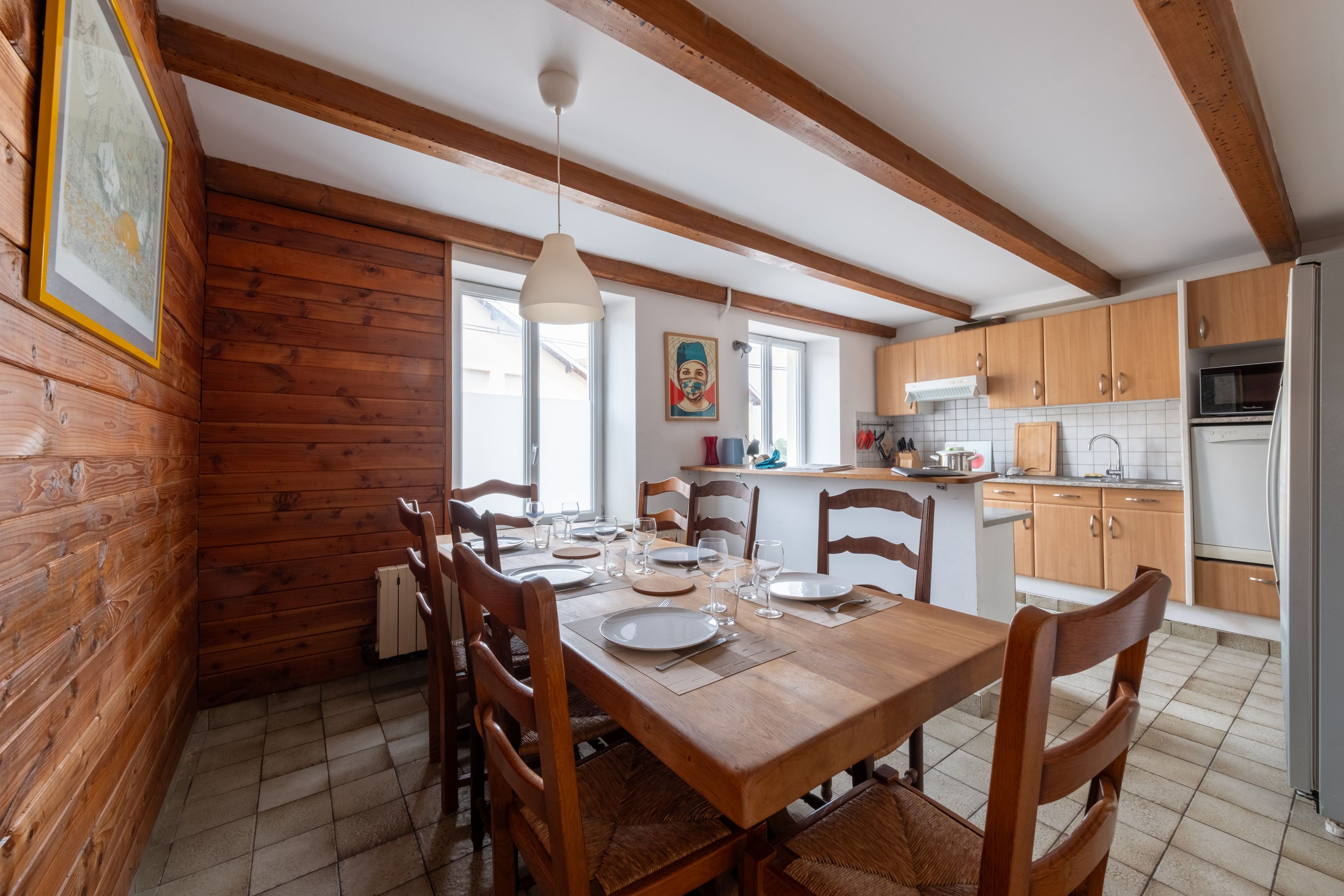 A wooden interior with a dining table set for six, kitchen cabinets, and a refrigerator.