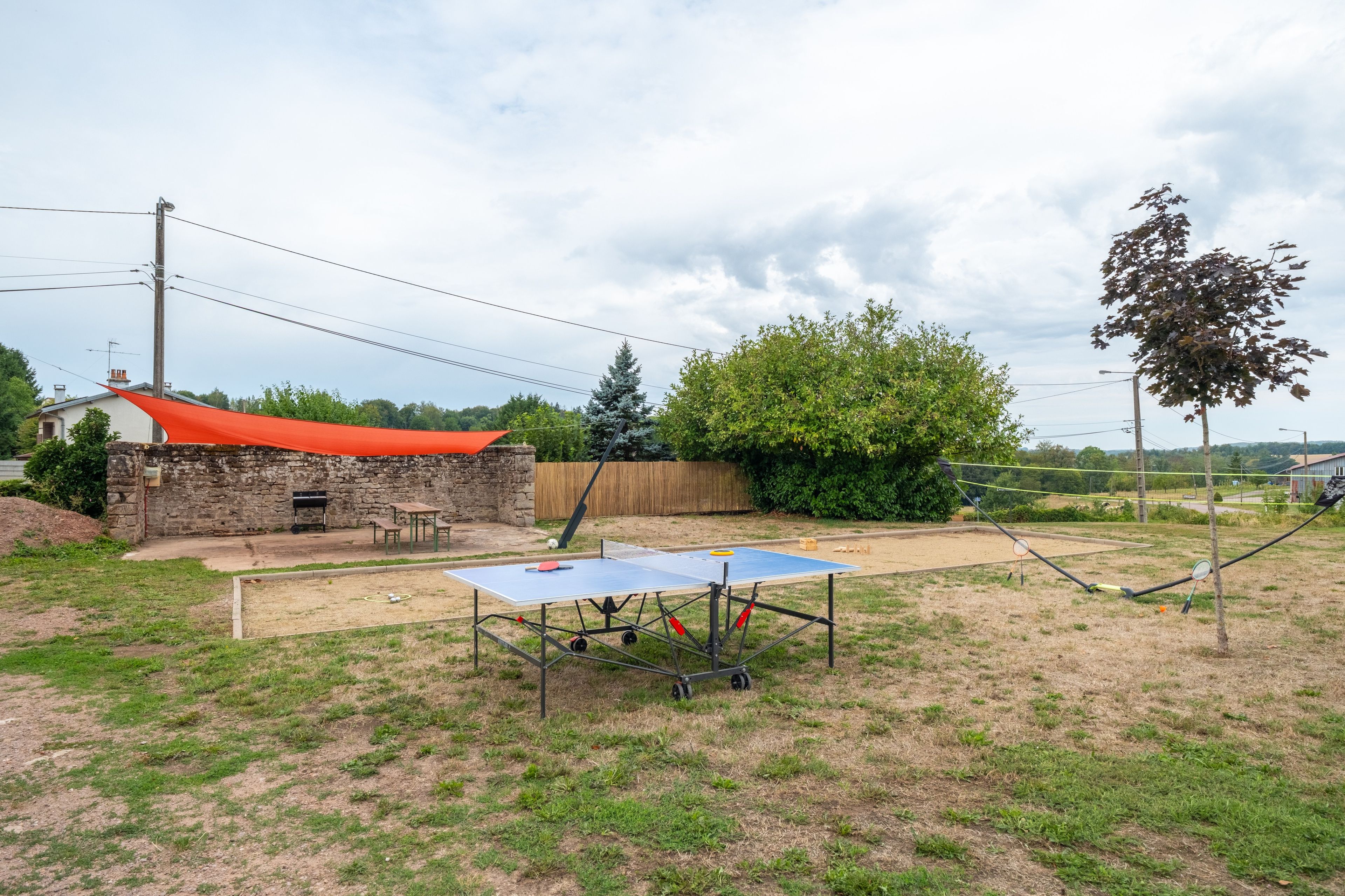 A backyard with a ping pong table, a stone barbecue area, and a wooden fence.