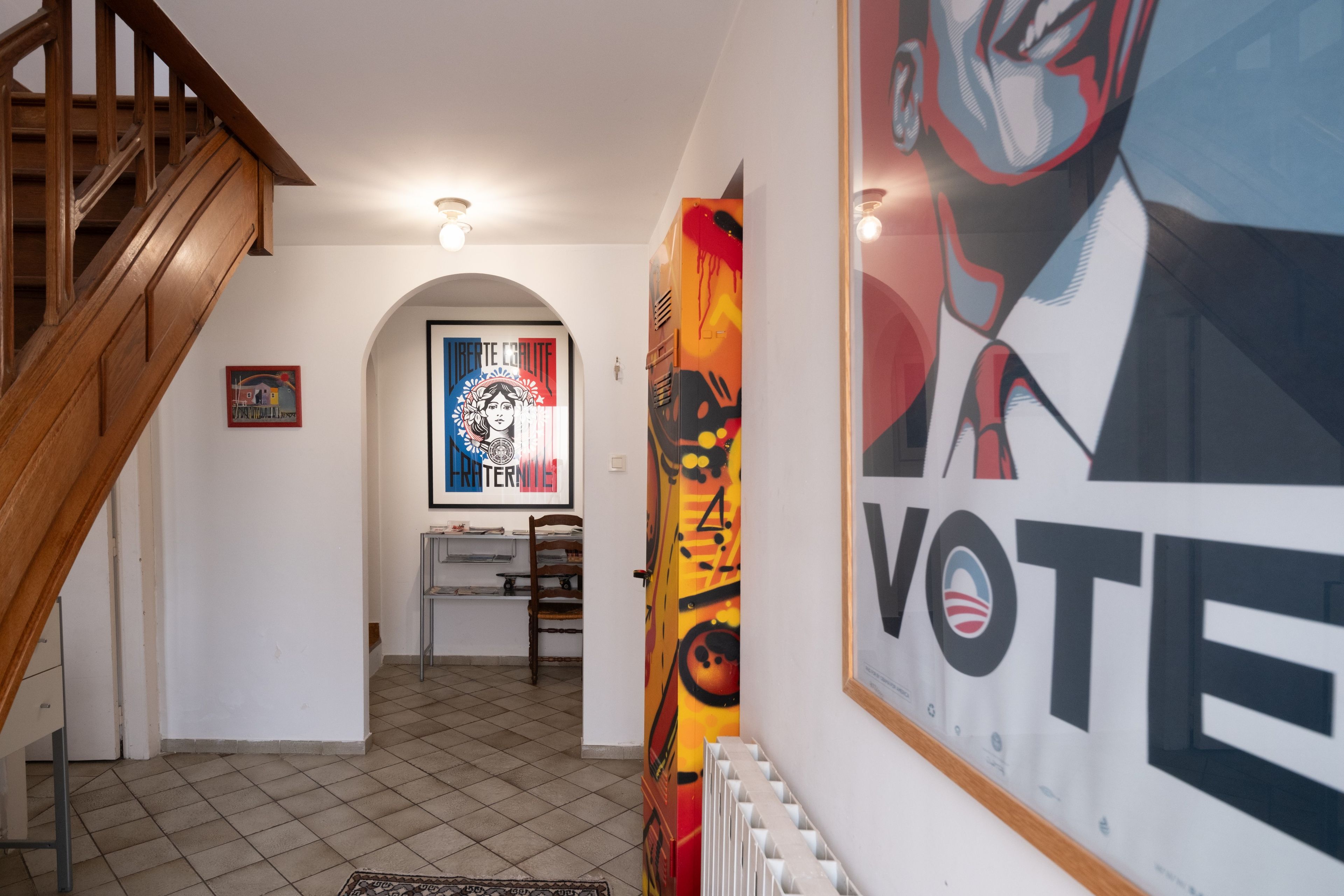 Un pasillo con una escalera de madera, un radiador y un cartel grande con la palabra 'VOTE'.