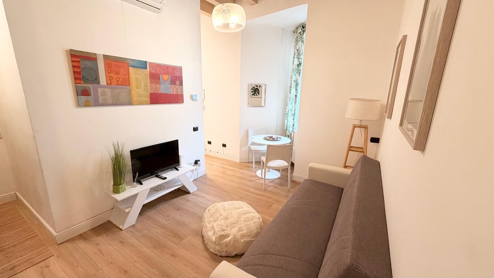 Een moderne woonkamer met een flatscreen televisie, een witte bank, een ronde salontafel en een kleine eettafel met stoelen.