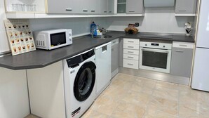 A compact kitchen with a washing machine, microwave, oven, and a coffee guide on the counter.