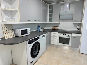 A compact kitchen with a washing machine, microwave, oven, and a coffee guide on the counter.