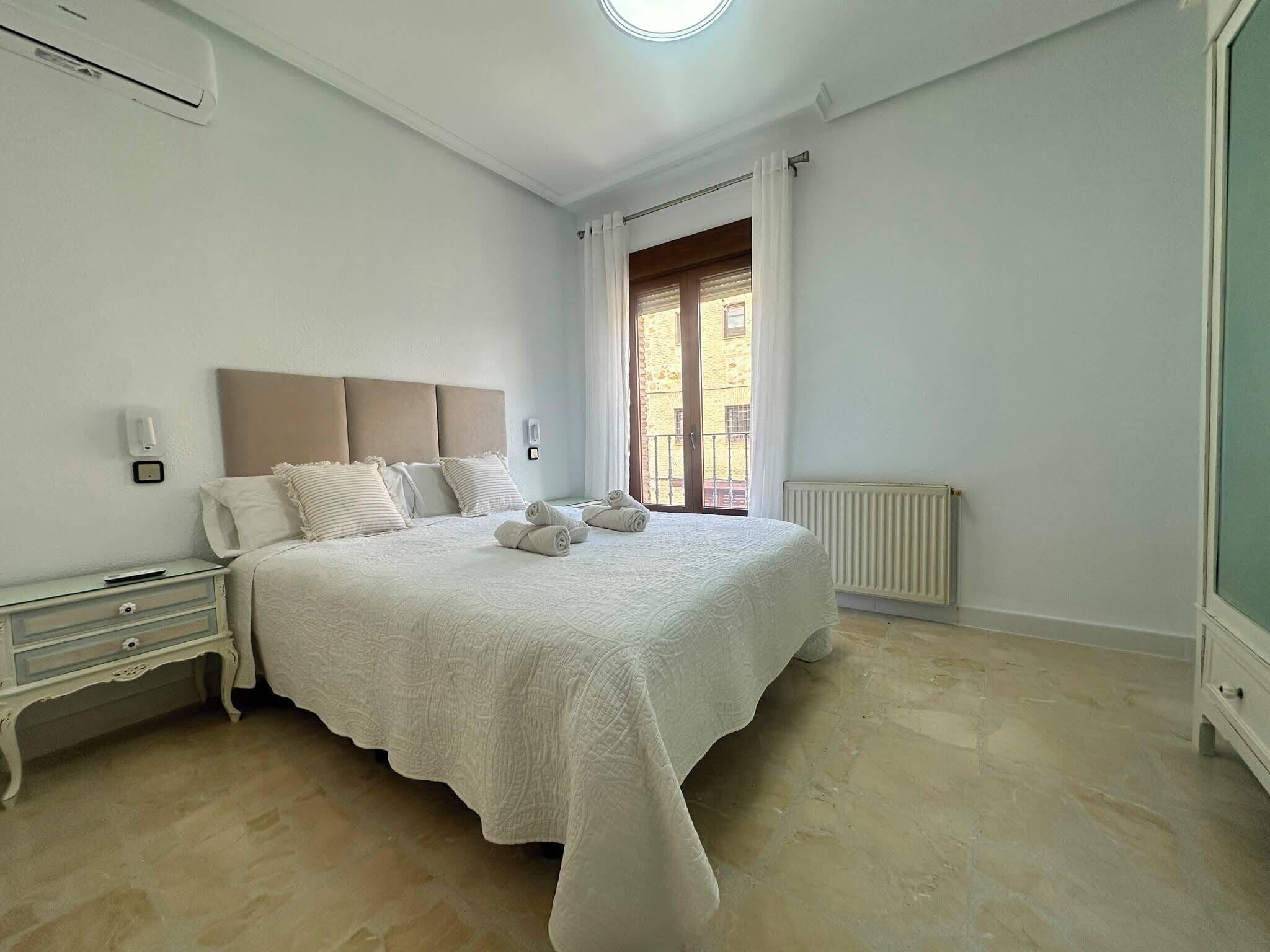 Une chambre à coucher avec un lit, des tables de chevet, un radiateur et une fenêtre avec des rideaux.
