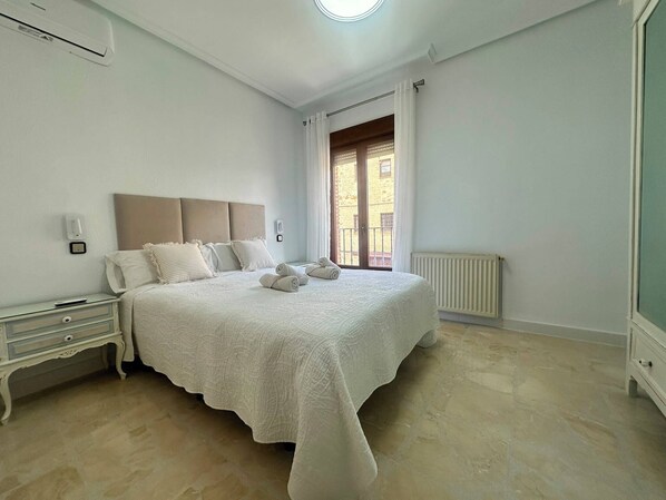 Un dormitorio con cama, mesitas de noche, radiador y ventana con cortinas.