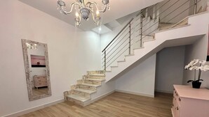 A staircase with marble steps leading to an upper floor, a chandelier, and a mirror with a rustic frame.