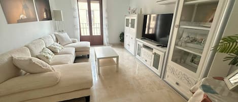 Una sala de estar con sofá, mesa de centro, televisor y aparador con puertas de vidrio.