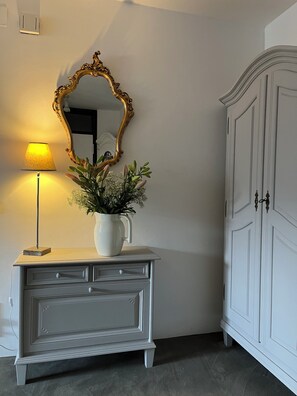 Ein weißer Schminktisch mit Spiegel und Lampe, eine Vase mit Blumen sowie ein weißer Kleiderschrank.