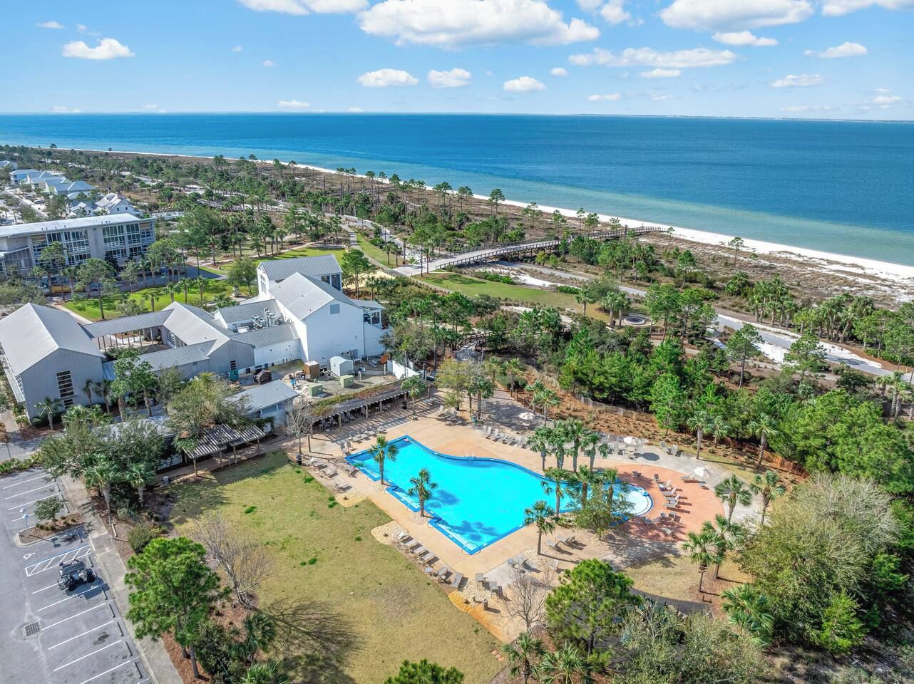 An aerial view of a resort with a swimming pool surrounded by palm trees and a beach in the background.