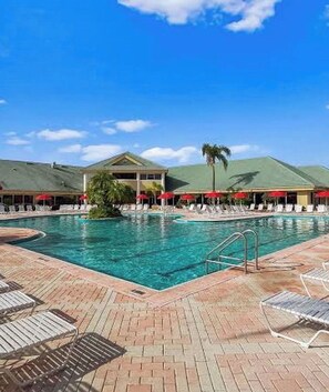 A pool area with lounge chairs and umbrellas, a clear sky, and a building with a green roof. - 2-bedroom hotel in pleasant Kissimmee with AC and Pools with bar + movie theater (Kissimmee)
