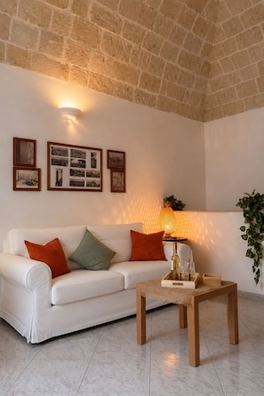 A living room with a white sofa, a wooden coffee table, and a lamp. There are framed pictures on the wall. - Just a short walk from the Cathedral, the Swabian Castle, the harbor, and downtown. (Trani)