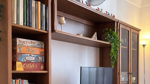 A wooden entertainment unit with a flat-screen TV, shelves with books and games, and a decorative fan. - Just a short walk from the Cathedral, the Swabian Castle, the harbor, and downtown. (Trani)