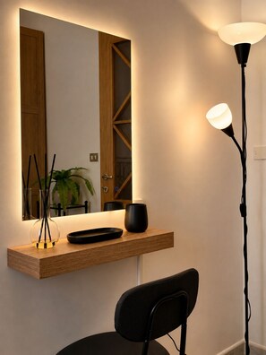 A modern room with a wooden desk, a black chair, a floor lamp, and a mirror reflecting a door and a plant.