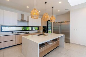 A modern kitchen with a central island, stainless steel appliances, and pendant lighting. - Oceanview Luxury Home in Pacifico Coastal Living (Coco)