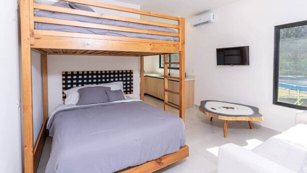 A bunk bed with a wooden headboard, a small round table, a white chair, and a TV mounted on the wall. - Oceanview Luxury Home in Pacifico Coastal Living (Coco)
