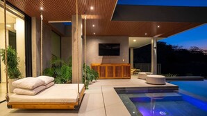 A modern outdoor living area with a pool, seating, and a wooden structure. - Oceanview Luxury Home in Pacifico Coastal Living (Coco)