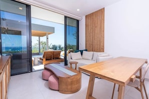 A modern living room with a wooden dining table, a sofa, and a seating area with cushions. - Oceanview Luxury Home in Pacifico Coastal Living (Coco)