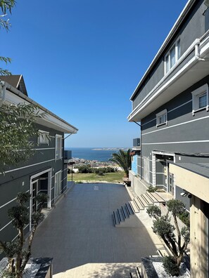 Edificio residencial con vista al mar, patio empedrado y un pequeño jardín.