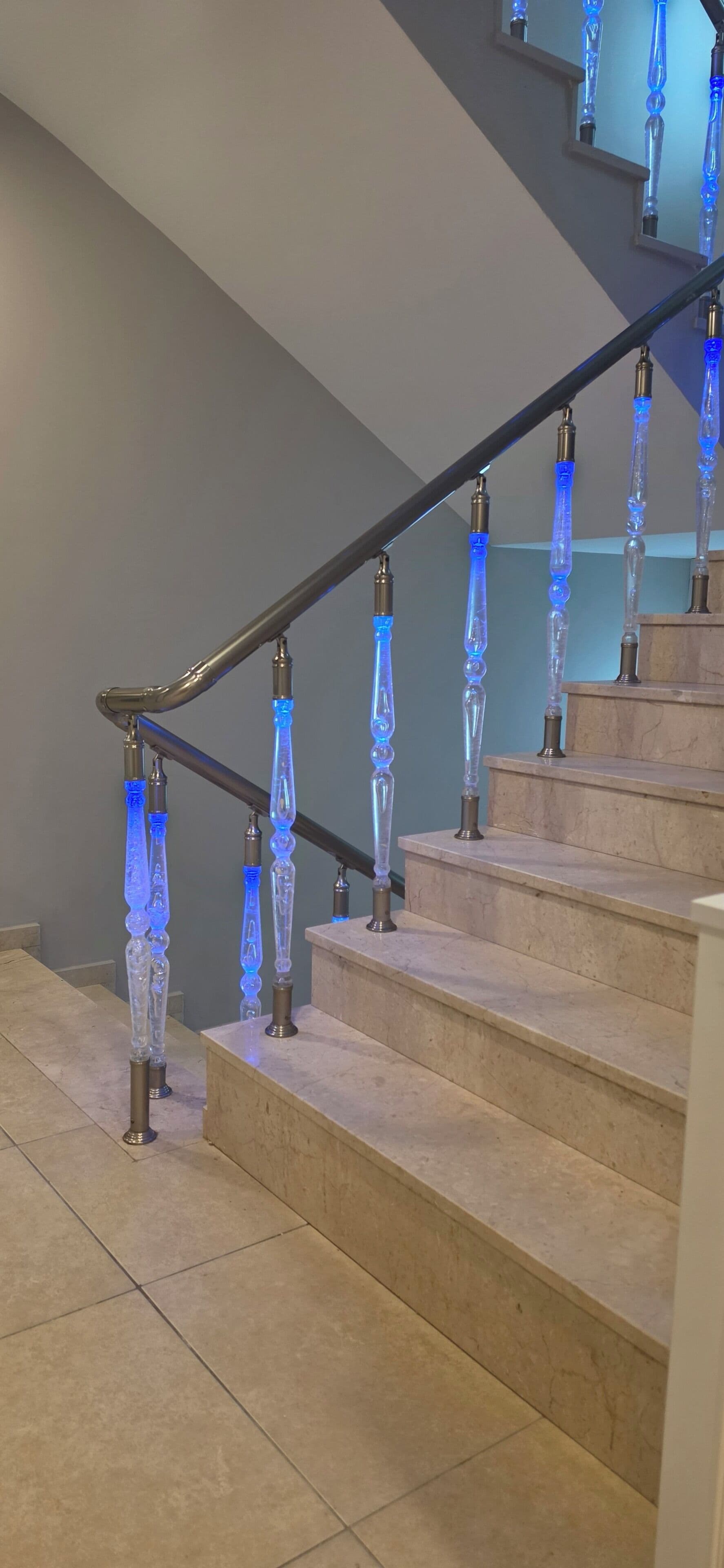 A staircase with a modern design, featuring a glass railing with blue lighting and a metal handrail.
