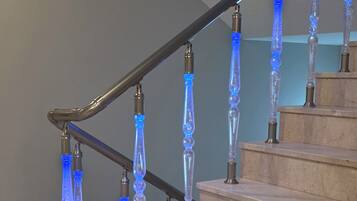 A staircase with a modern design, featuring a glass railing with blue lighting and a metal handrail.