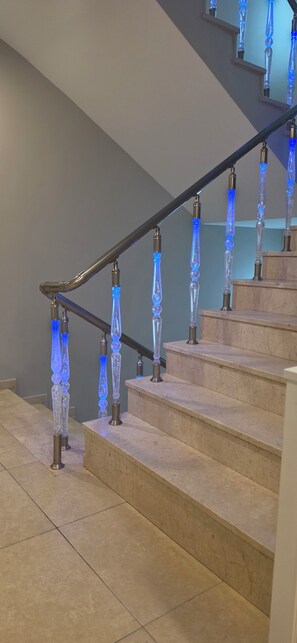 Una escalera de diseño moderno, con barandilla de vidrio iluminada en azul y pasamanos de metal.