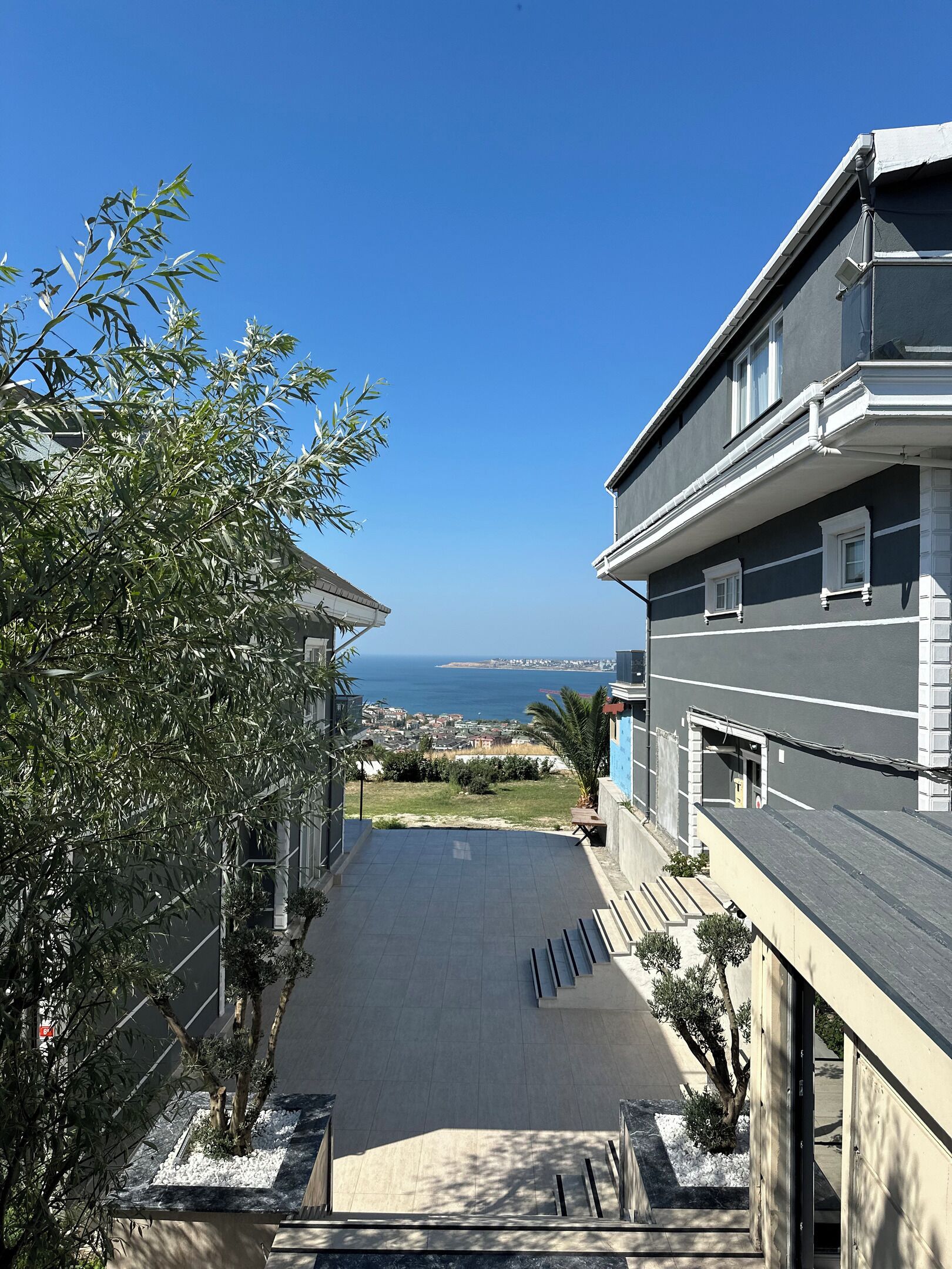 A residential building with a view of the sea, a paved driveway, and a small garden area.