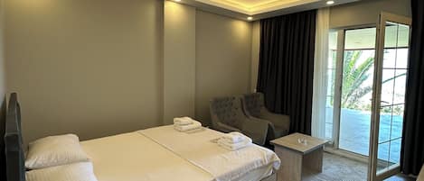 A modern hotel room with a large bed, a small sofa, a coffee table, and a view of the outdoors.