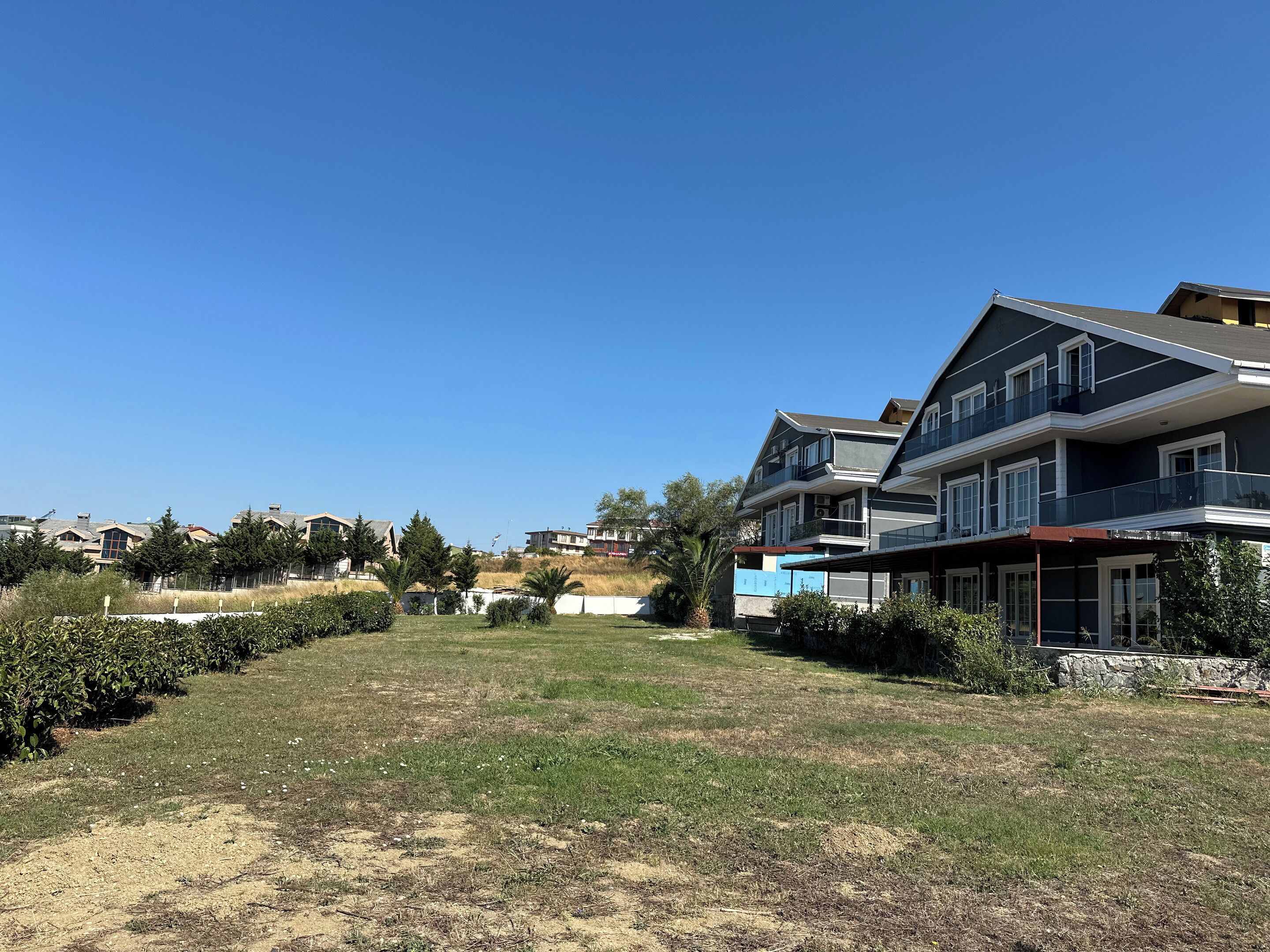 A residential area with a large two-story house featuring a balcony, a grassy lawn, and a clear blue sky.