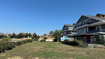A residential area with a large two-story house featuring a balcony, a grassy lawn, and a clear blue sky.