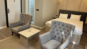 Una habitación de hotel con una cama, dos sillones, una mesita y suelo de madera.