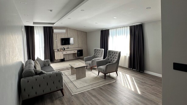 Un amplio salón con un sofá, sillones, una mesa de centro y un televisor sobre un mueble de madera.