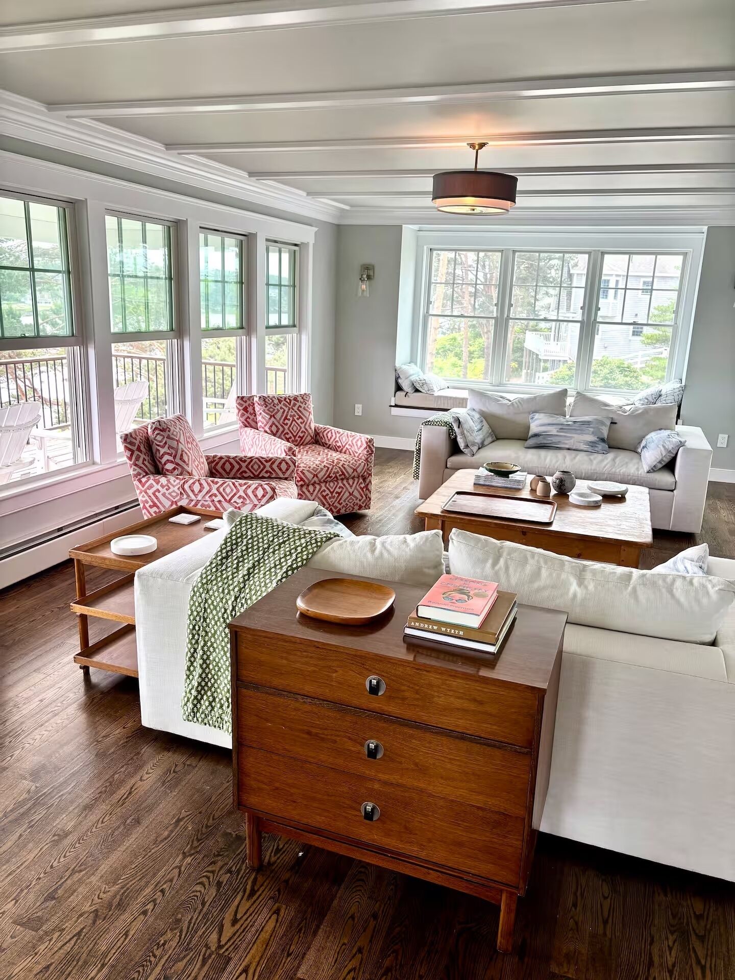 A spacious living room with a wooden floor, a white sofa, a red patterned armchair, and a wooden coffee table.
