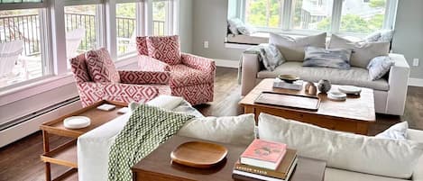 A spacious living room with a wooden floor, a white sofa, a red patterned armchair, and a wooden coffee table.