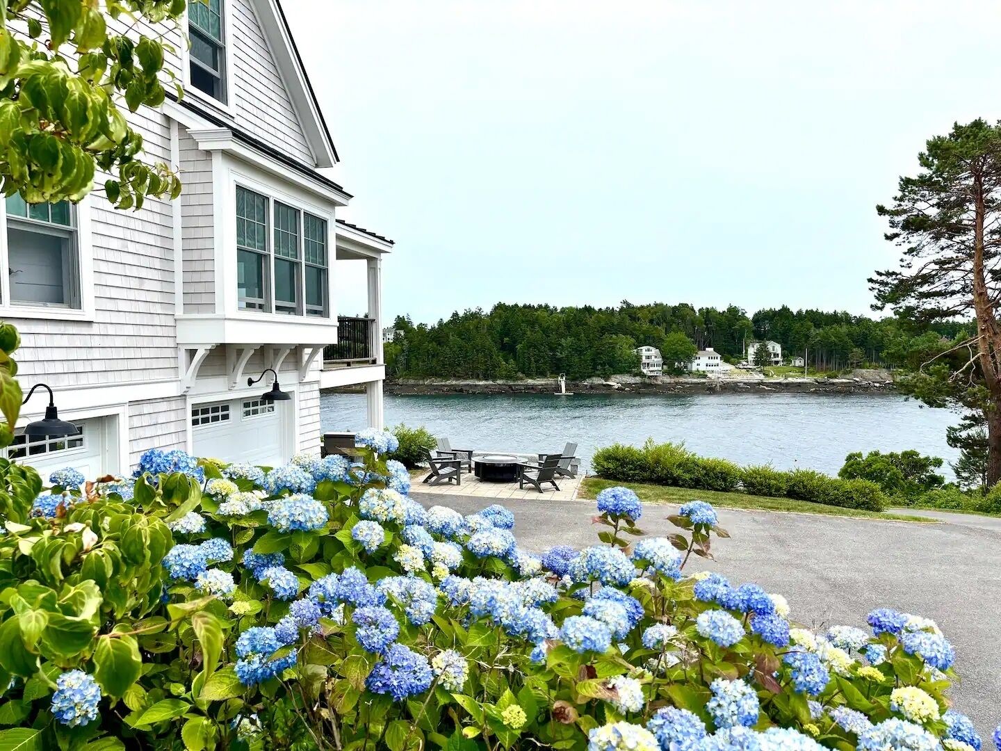 A waterfront property with a two-story building, outdoor seating, and a view of the water.