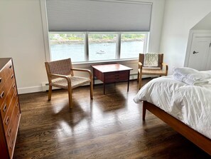 A bedroom with a wooden floor, a bed, two wicker chairs, a small wooden table, and a window with a view of a body of water. - Ocean front Home with Private dock - Winter rental Available (Harpswell)