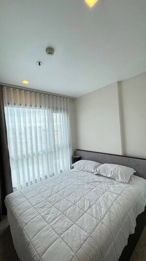 Ein Hotelzimmer mit einem großen Bett, einem Fenster mit Vorhängen und einer Deckenleuchte.