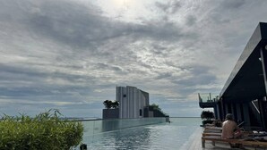 Ein Infinity-Pool auf dem Dach mit Blick auf ein modernes Gebäude und einen bewölkten Himmel.