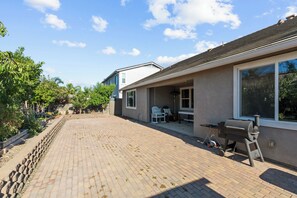 Ein Wohnhaus mit einer gepflasterten Terrasse, Sitzgelegenheiten im Freien und einem Grill.
