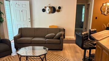 A living room with a sofa, a coffee table, a chair, a dining area with a bar, and a ceiling fan.