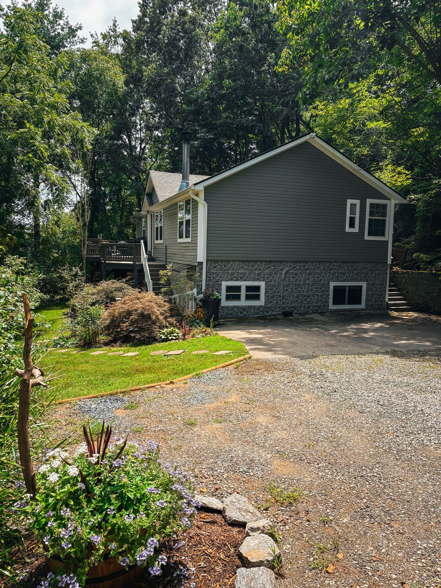 A two-story house with a stone foundation, a front porch, and a gravel driveway.