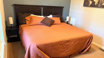 A neatly made bed with an orange bedspread and two pillows, a bedside table with a lamp, and a world map on the wall.
