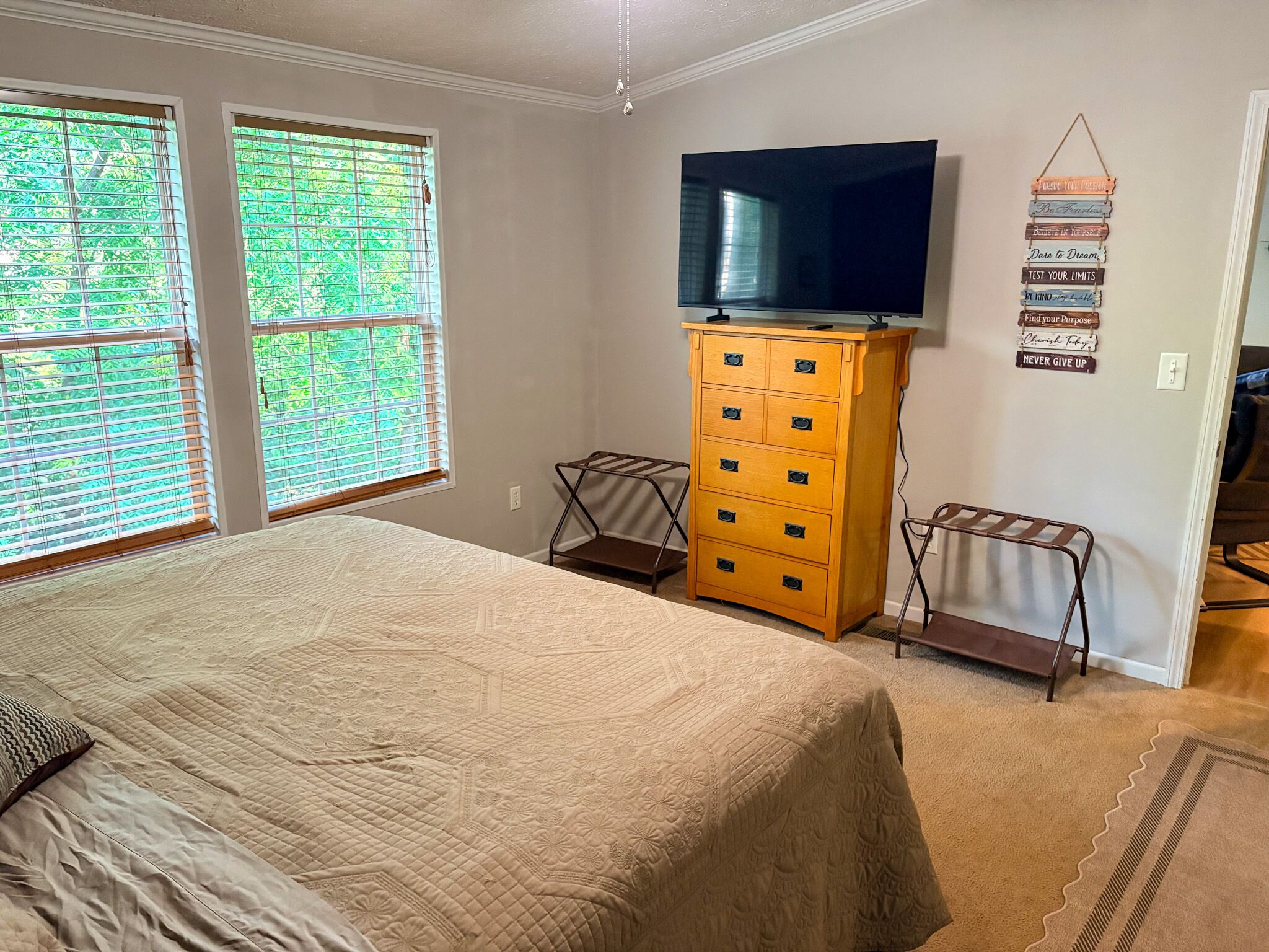 A bedroom with a bed, a dresser, a television, and a wall with motivational quotes.