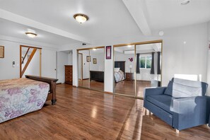 A bedroom with a wooden floor, a bed with a floral bedspread, a blue sofa, a large mirror, and a wardrobe.